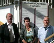 Zwei Herren und eine Frau stehen vor einer Infotafel der Stadtverwaltung in Hilden