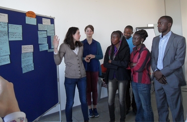 Studenten aus Deutschland und Afrika schauen sich gemeinsam eine Flipchart mit Plakaten an.