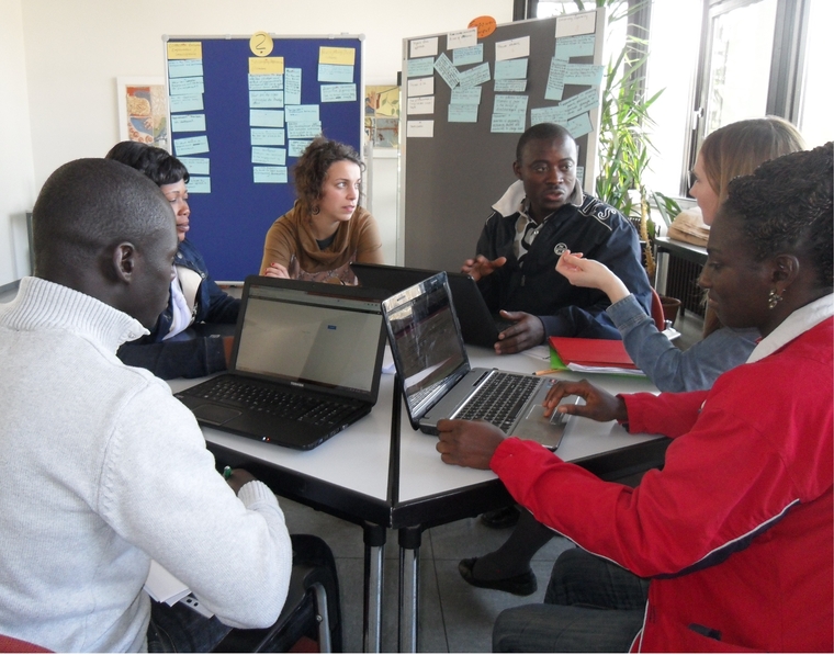Studenten aus Afrika und Deutschland sitzen gemeinsam an einem Tisch und diskutieren vor geöffneten Laptops.