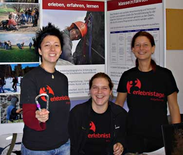 Drei junge Frauen mit Erlebnistage-T-Shirts stehen vor Infownden