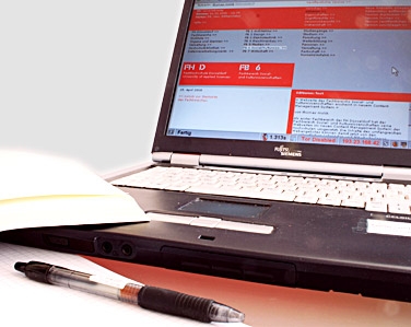 Laptop mit dem ZWeC-System, Buch, Block und Stift auf einem Schreibtisch