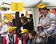 Kinder mit gelben Mützen des Stöbertages sitzen mit einem Studierenden vor einem Zelt.