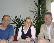 3 Personen sitzen an einem Tisch und lächeln fröhlich in die Kamera. Links sitzt der neue Dekan Prof Dr. Hubert Minkenberg in einem blauen Polo-Shirt. In der Mitte Prof. Dr. Charlotte Hanisch (Prodekanin) in einer weissen Bluse mit schwarzer Weste. Rechts sitzt Prof. Dr. Walter Eberlei (Prodekan) in einem blau-weiss gestreiftem Hemd und trägt dazu ein sandfarbenes Jacket.
