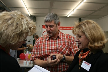 Zwei blonde Frauen im Gespräch mit einem Mann in rot-kariertem Hemd.