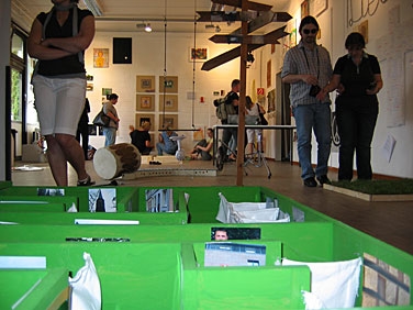 Kunstausstellung mit einem grünen Labyrinth auf dem Boden und weiteren Exponaten im Hintergrund