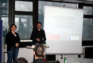 Anne van Rießen und Dr. Christian Bleck, wissenschaftliche Mitarbeiter im Projekt SORAQ, stehen vor einer Leinwand mit aufgelegter Powerpoint-Präsentation