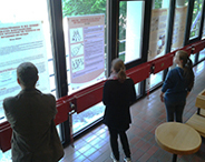 Das Vorschaubild zeigt Studierende, die die Ausstellungsplakate im Foyer des FB6 betrachten.