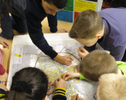Das Vorschaubild zeigt einen Fotoausschnitt, auf dem Kinder über einen Stadtplan gebeugt in diesem mehrere Punkte markieren