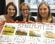 Drei junge Frauen halten ein Plakat mit der Aufschrift Spielplätze und mit Fotos