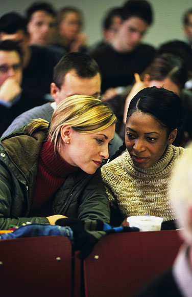 Eine europische und eine afrikanische Studentin sitzen zusammen im Hrsaal und stecken die Kpfe zusammen