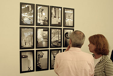 Zwei Menschen beim Betrachten einer Gruppe von Fotos an einer Wand