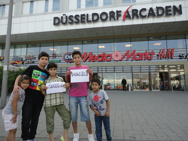 Fünf Kinder stehe vor dem Eingang der Düsseldorfer Arcaden. Zwei Kinder halten kleine Plakate hoch. Auf dem ersten steht das Wort "chillen" und auf dem zweiten "Mall".